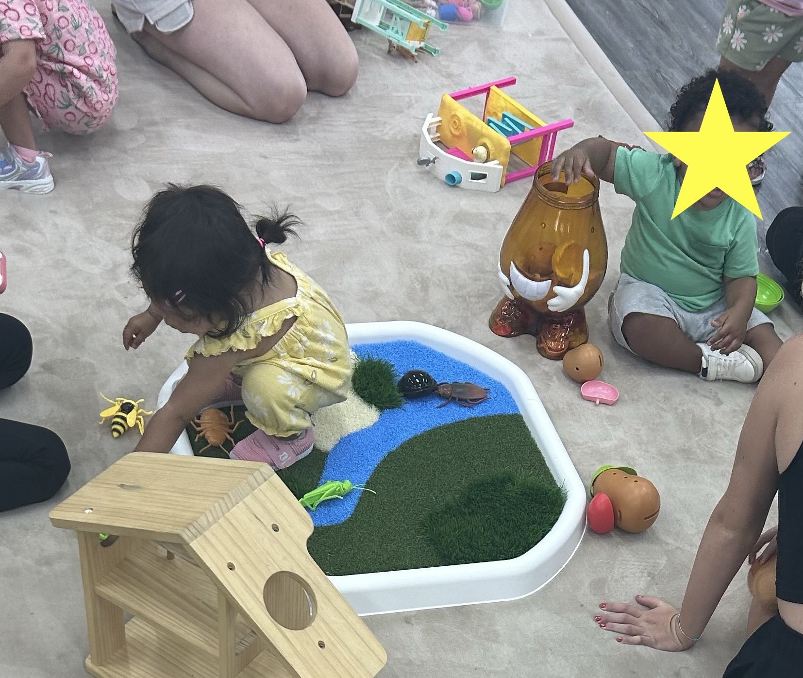 Children exploring pretend play around a small white Meka Tuff Tray, with one child's face covered by a yellow star