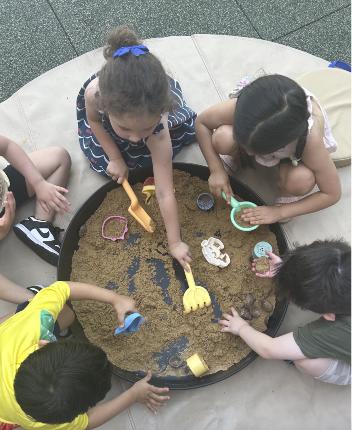 Children gathered around a large sensory tray playing together with sand and scoops at a WonderPlay program.
