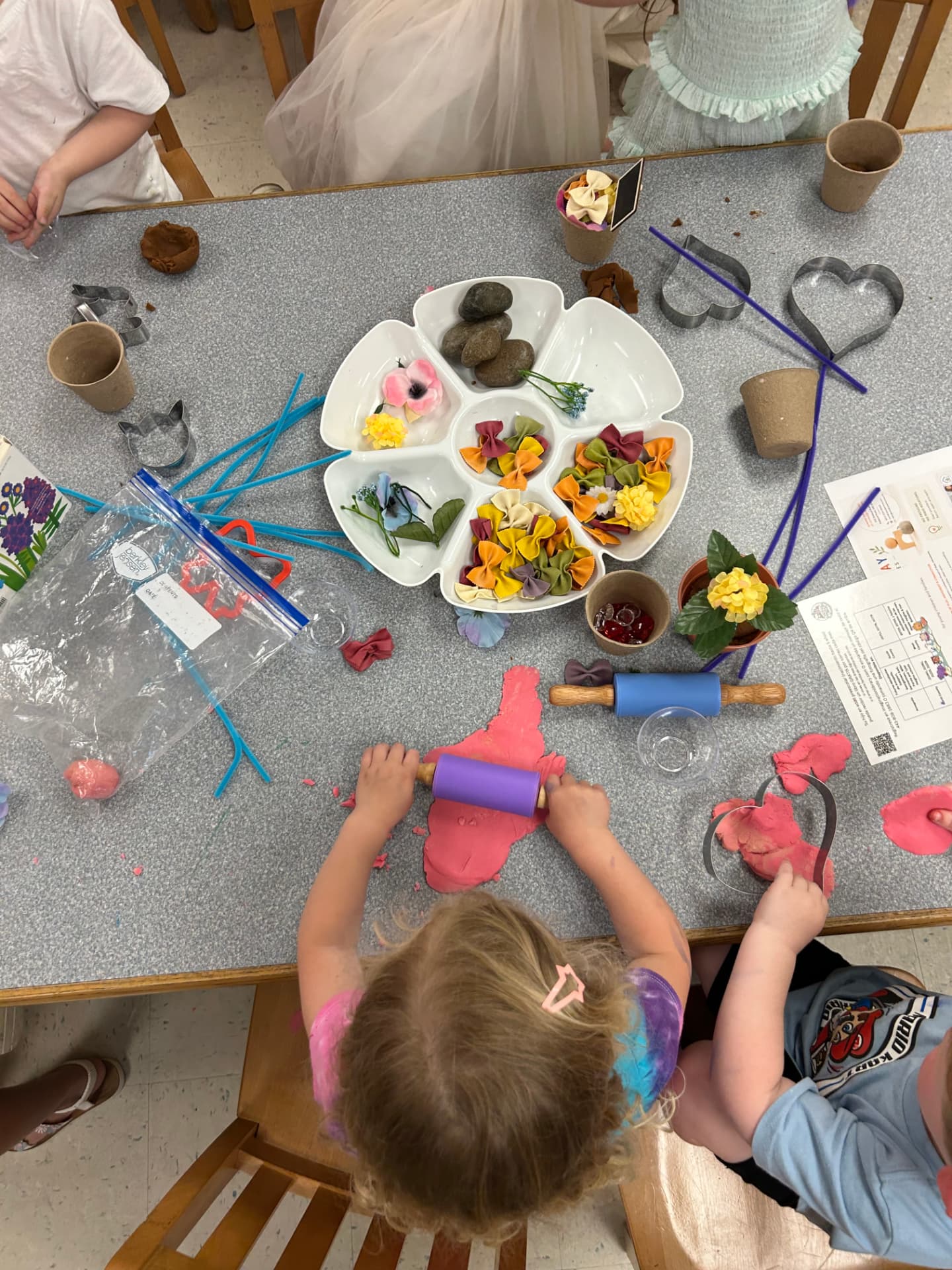 A child rolling pink dough with a small rolling pin at a WonderPlay sensory table