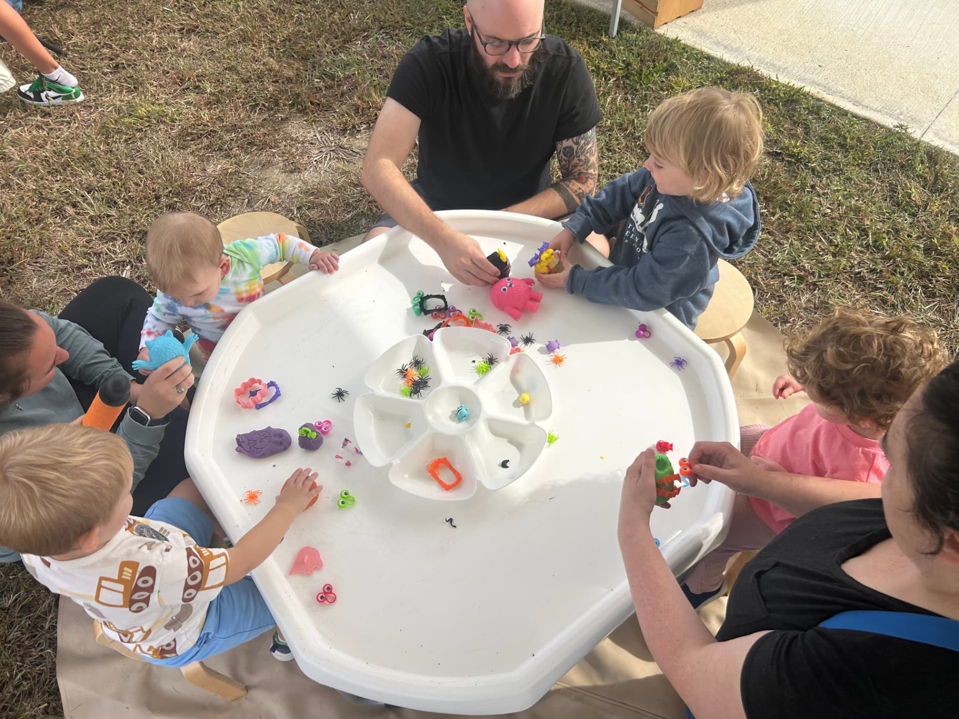 Children and adults gathered around an outdoor WonderPlay sensory table, playing together