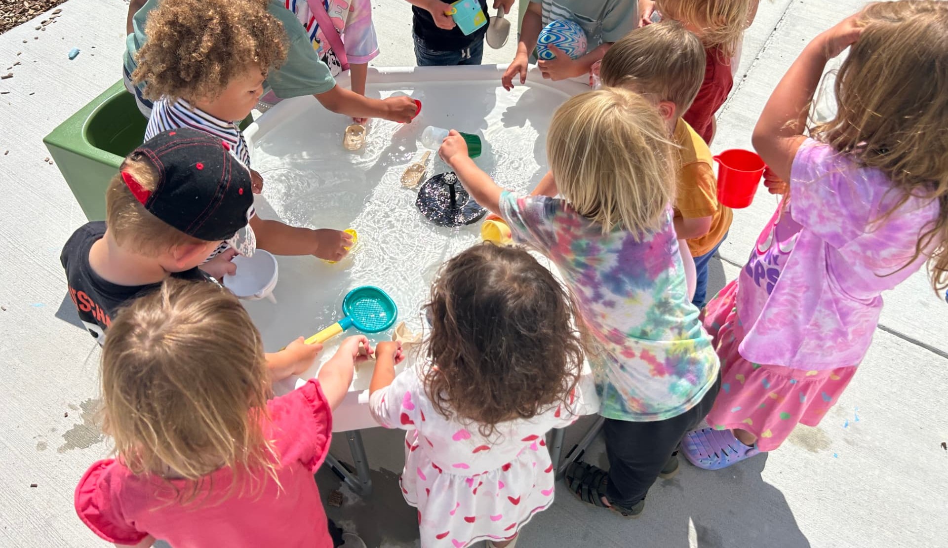 Children gathered around an outdoor water table playing with cups and scoops
